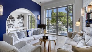 Ein geräumiges Wohnzimmer mit einem weißen Sofa, einem runden Couchtisch und einem großen Fenster mit Blick ins Freie.