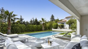 Ein moderner Außenbereich mit Pool, weißer Möbel und einem gepflegten Garten.