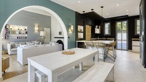 Ein modernes Wohnzimmer mit einem weißen Sofa, einem Essbereich mit Tisch und Stühlen in Weiß sowie einer Küche mit schwarzen Schränken und einer weißen Arbeitsplatte.