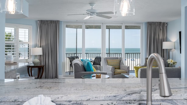 A spacious living room with a large window overlooking the sea, a ceiling fan, and a marble floor. - Gullwing 505 3BR Oasis: Beachfront & Lanai (Fort Myers Beach)