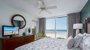 A bedroom with a bed, a TV, a dresser, a ceiling fan, a window with a beach view, and a chair. - Gullwing 505 3BR Oasis: Beachfront & Lanai (Fort Myers Beach)