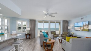 A spacious living room with a balcony, a ceiling fan, and a large window overlooking the ocean. - Gullwing 505 3BR Oasis: Beachfront & Lanai (Fort Myers Beach)