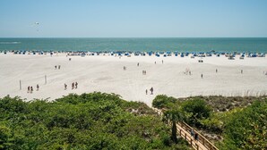 A beach with a wooden walkway leading to the sea, surrounded by dense greenery. - Gullwing 505 3BR Oasis: Beachfront & Lanai (Fort Myers Beach)