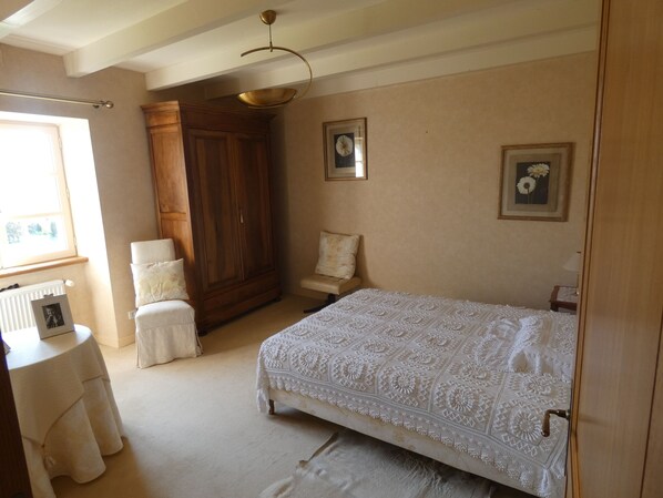 Un dormitorio con una cama grande, un armario de madera, una mesita y una silla.