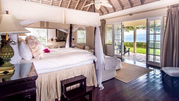 Ett rymligt sovrum med en stor säng, en takfläkt och utsikt över omgivningarna genom en skjutdörr i glas.