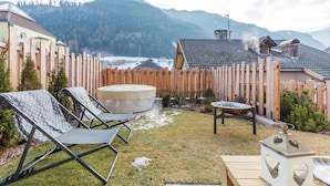 Un patio trasero con cerca de madera, sillas de descanso, bañera de hidromasaje y terraza de madera.