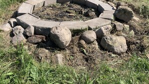 A circular stone fire pit surrounded by rocks in a grassy field.