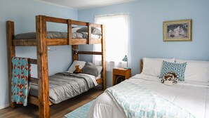 A room with a bunk bed, a single bed, a nightstand, a lamp, and a framed picture on the wall.
