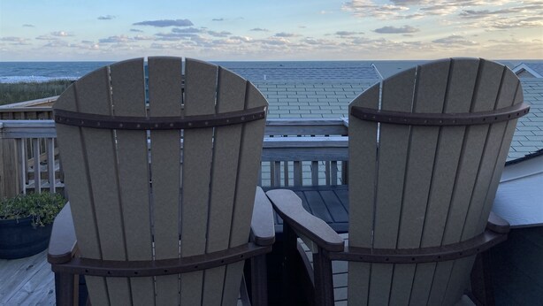 Twee Adirondack-stoelen kijken uit op een houten terras met uitzicht op de oceaan en een bewolkte lucht.