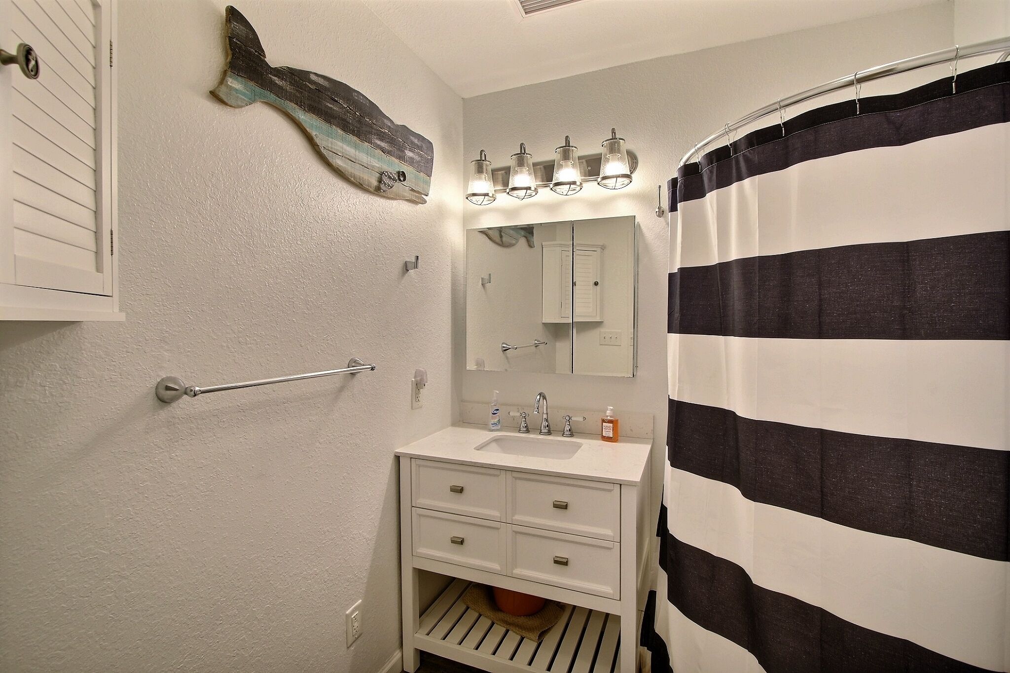 A bathroom with a white vanity, a mirror, a striped shower curtain, and a towel rack.