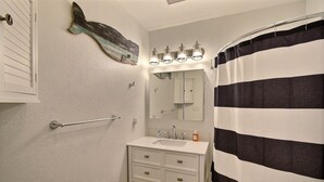 Een badkamer met een witte wastafel, een spiegel, een gestreept douchegordijn en een handdoekrek.