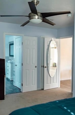 Quarto com ventilador de teto, portas brancas e uma cama.