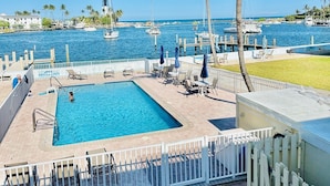 A swimming pool with a view of the sea and boats, surrounded by palm trees and a white fence.
