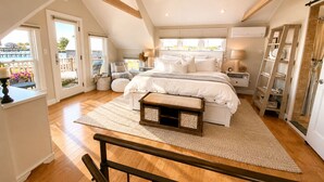 Un dormitorio con una cama grande, un banco de madera, una mesita de noche y vistas al exterior.