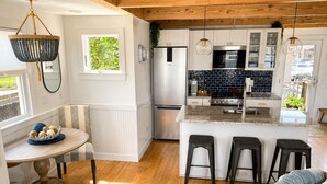 Una cocina moderna con armarios blancos, una isla central con taburetes y un refrigerador de acero inoxidable, además de una lámpara colgante.