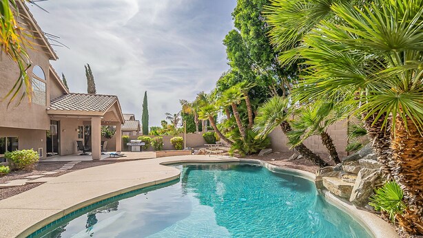 A swimming pool with a curved edge, surrounded by a landscaped area with palm trees and a building with a tiled roof. - Very Large 5br, Arrowhead Ranch, Games, Quiet, Relaxing (Glendale)