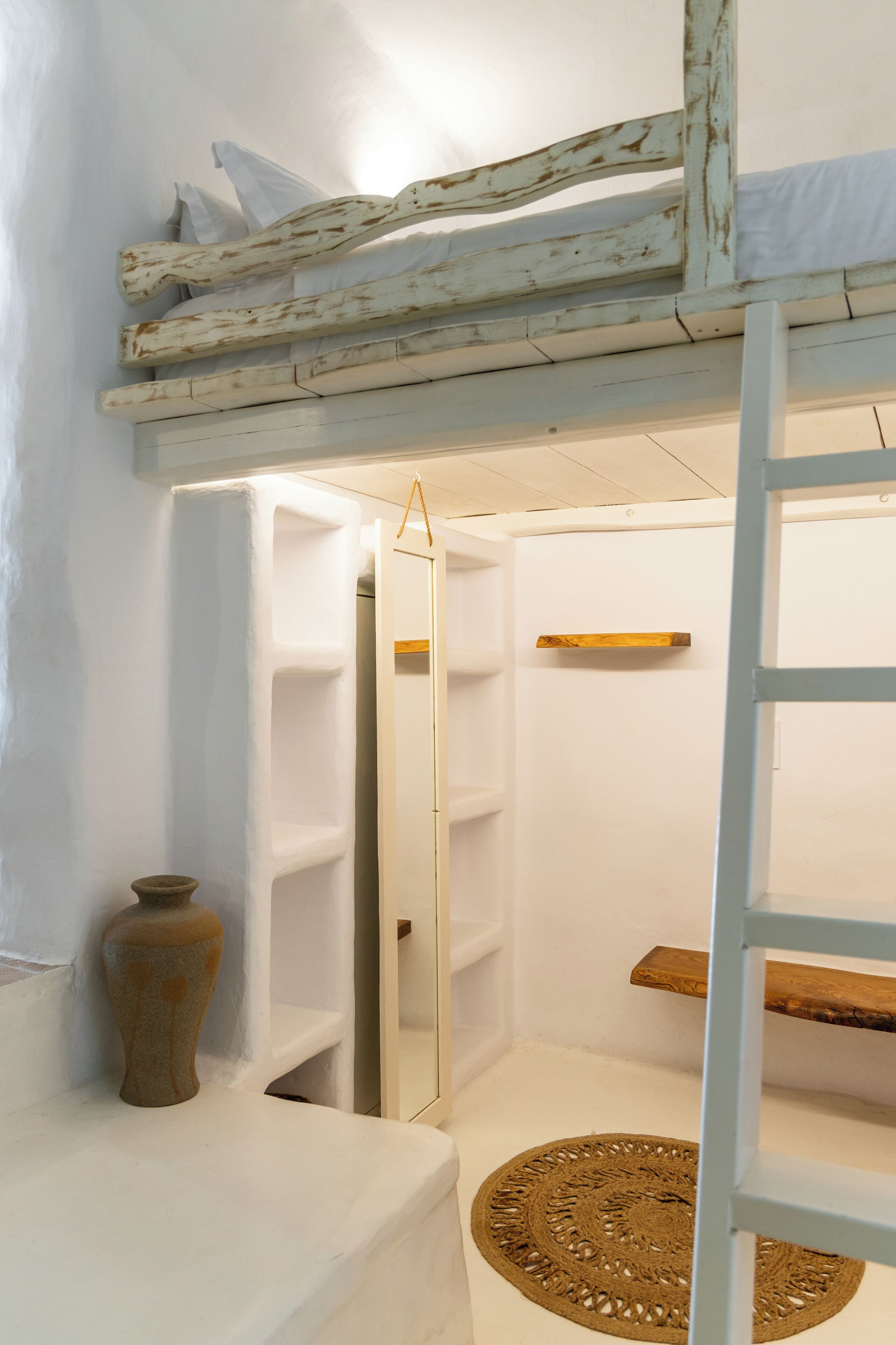Quarto compacto com beliche, prateleira pequena, tapete de palha e um vaso.