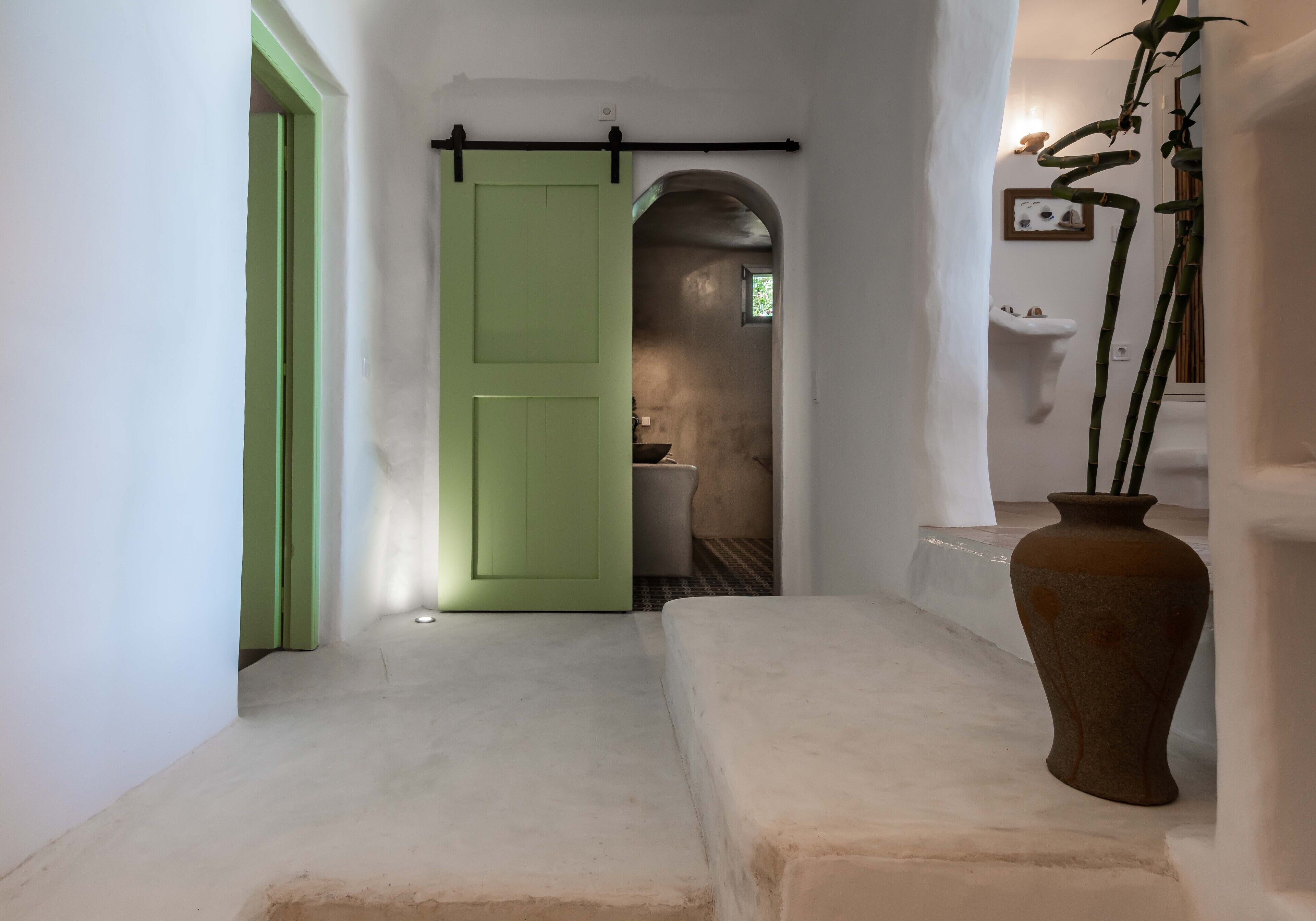 Un pasillo con una puerta verde, un banco blanco y un jarrón grande con plantas.
