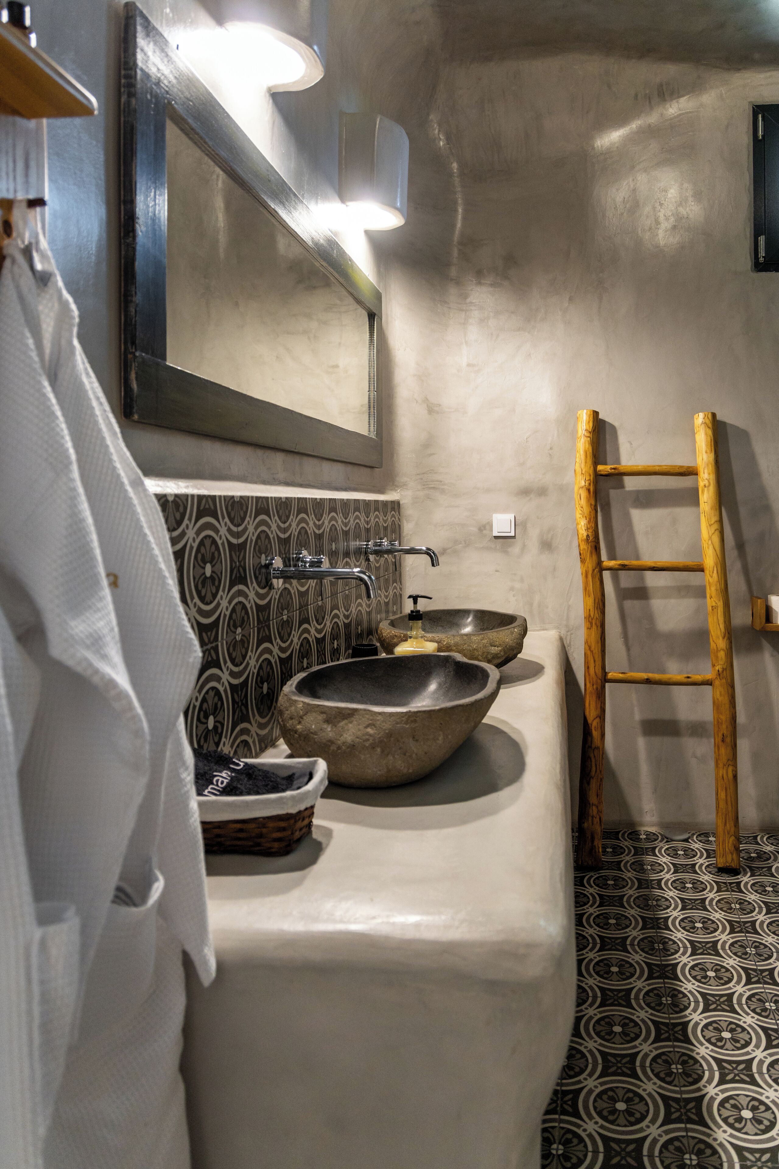 Une salle de bain dotée d’un grand miroir, de deux vasques en pierre, d’une échelle en bois et de carreaux de sol à motifs.