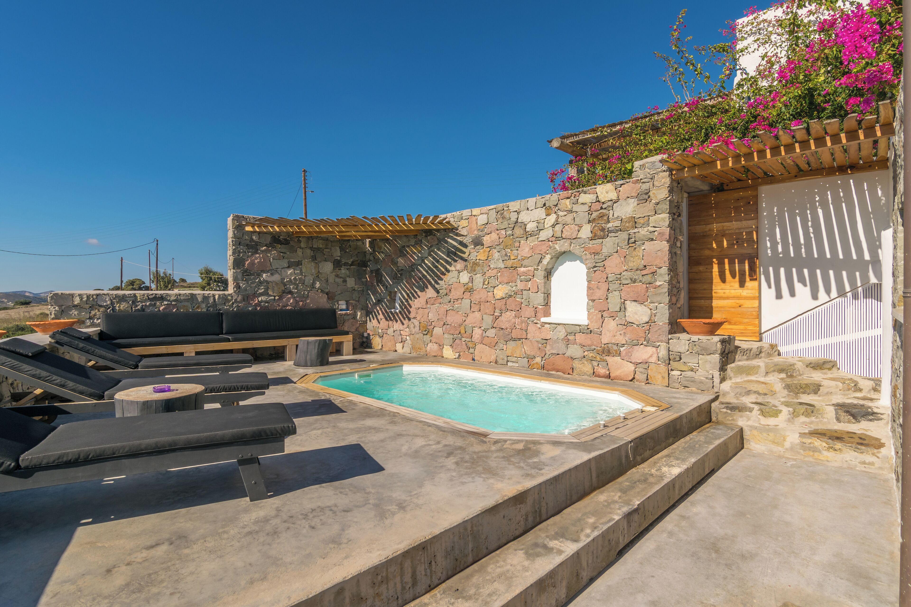 Un área de piscina en la azotea con muros de piedra, una pérgola de madera y mobiliario exterior.