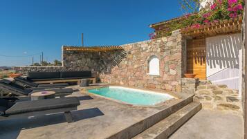 Un área de piscina en la azotea con muros de piedra, una pérgola de madera y mobiliario exterior.
