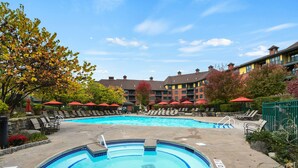A swimming pool with lounge chairs and umbrellas, surrounded by multi-story buildings with balconies.