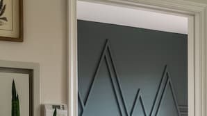 A bedroom with a bed, a potted plant, and a wall-mounted thermostat.