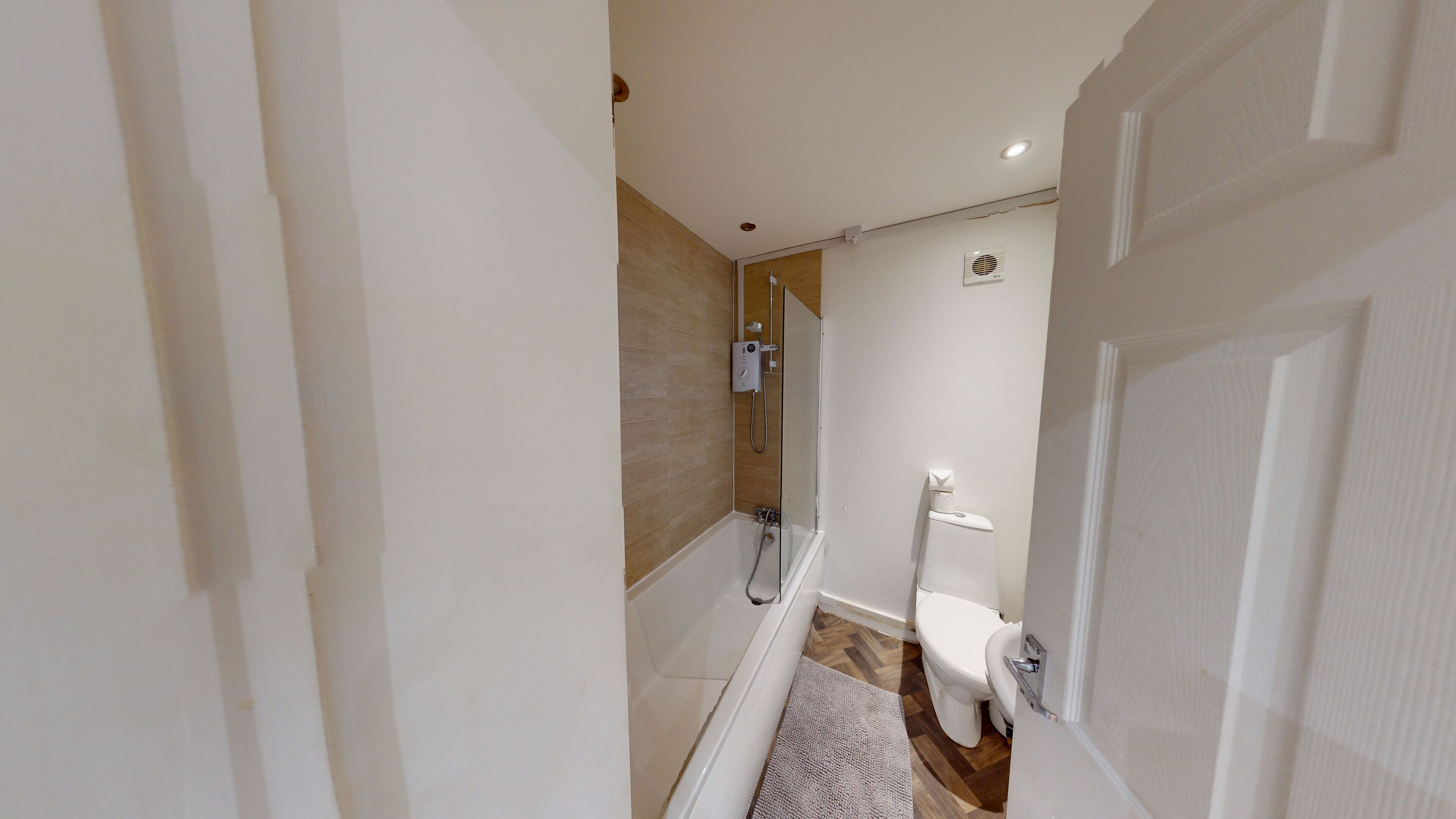 A narrow hallway leading to a bathroom with a shower, toilet, and a small rug on the floor.