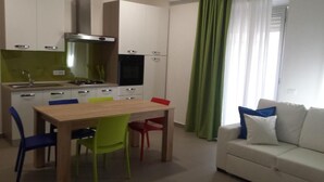 A compact kitchen with a dining table and chairs, a sofa, and a window with curtains.