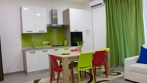 A modern kitchen with white cabinets, a green backsplash, and a dining area with a wooden table and colorful chairs.