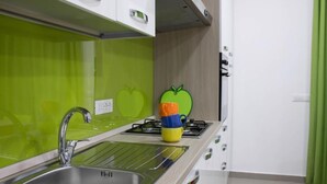 A kitchen with a stainless steel sink, a green backsplash, and a colorful apple-shaped object on the countertop. - Family three-room apartment (Catania)