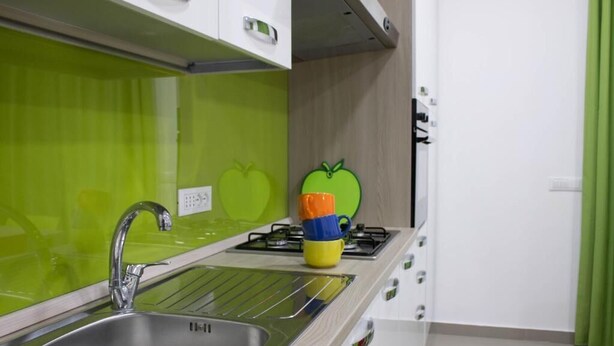 A kitchen with a stainless steel sink, a green backsplash, and a colorful apple-shaped object on the countertop.