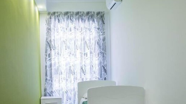 A narrow room with two beds, a window with curtains, and a white air conditioning unit on the wall. - Family three-room apartment (Catania)