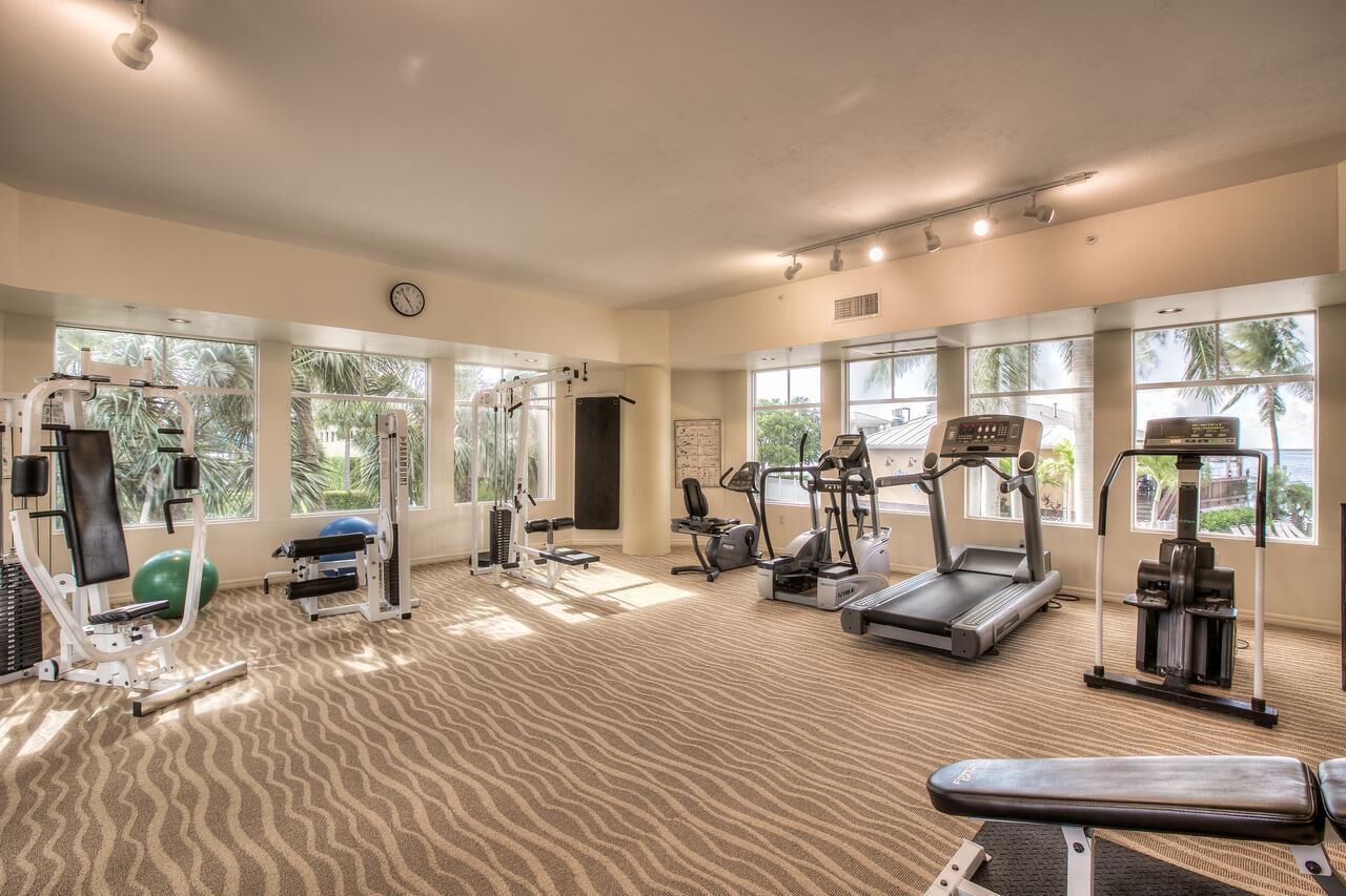 A spacious gym with various exercise equipment, large windows, and a carpeted floor.