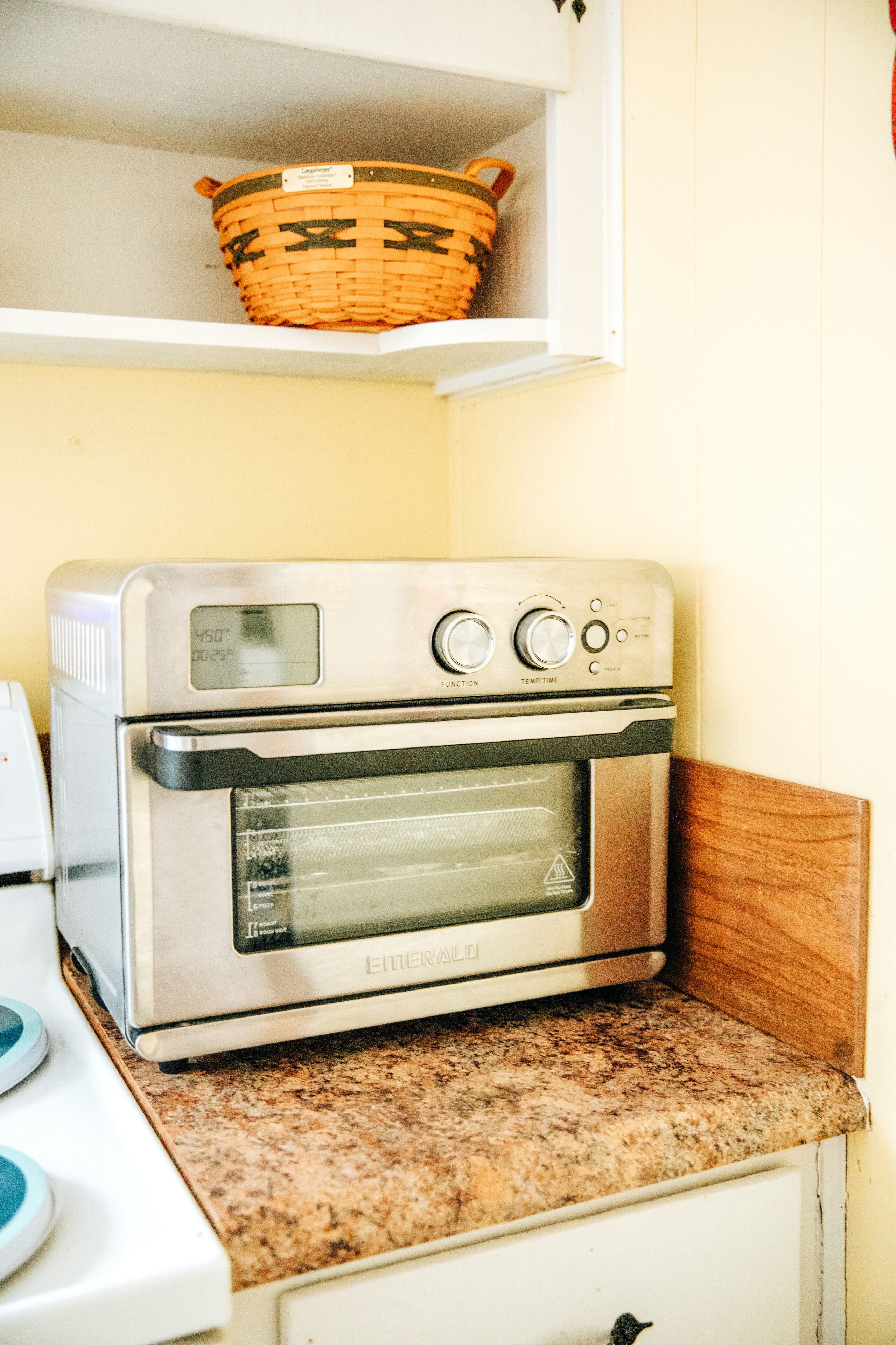 A kitchen with a stainless steel oven, a wooden shelf with a basket, and a granite countertop.
