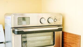 A kitchen with a stainless steel oven, a wooden shelf with a basket, and a granite countertop.