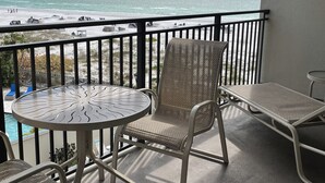 A balcony with a view of the beach and ocean. There are two wicker chairs and a small round table.