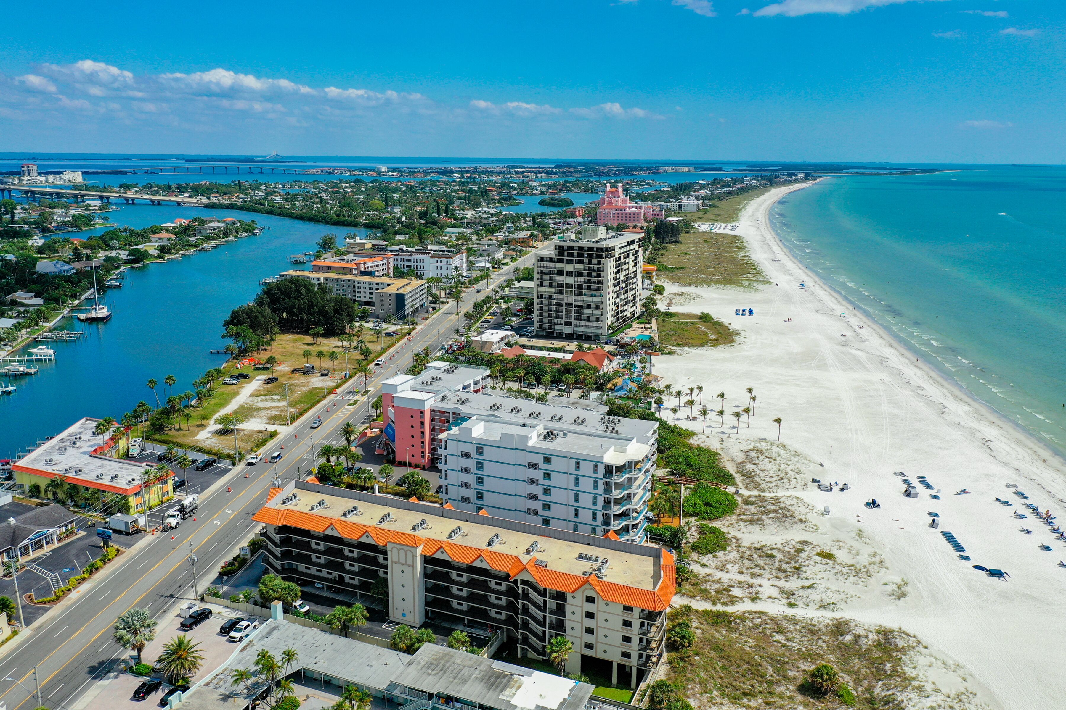 Vista aérea de una ciudad costera con un puerto deportivo, una playa y varios edificios de varios pisos con balcones.