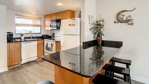 A modern kitchen with wooden cabinets, a black countertop, and a dining area with a bench.