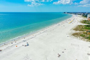A wide beach with clear turquoise water, a long stretch of sandy shore, and a few buildings in the background. - Beachfront condo on the Gulf of Mexico (St. Pete Beach)