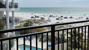 A beach view from a balcony with a pool, lounge chairs, and umbrellas.