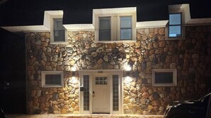 Una casa de piedra de dos pisos con una puerta blanca y varios ventanales, incluyendo un ventanuete.