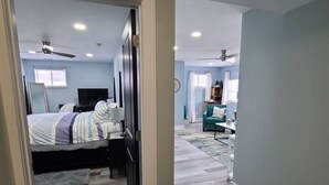 Un dormitorio con cama, escritorio y silla, un pasillo que conduce a otra habitación, y un ventilador de techo.