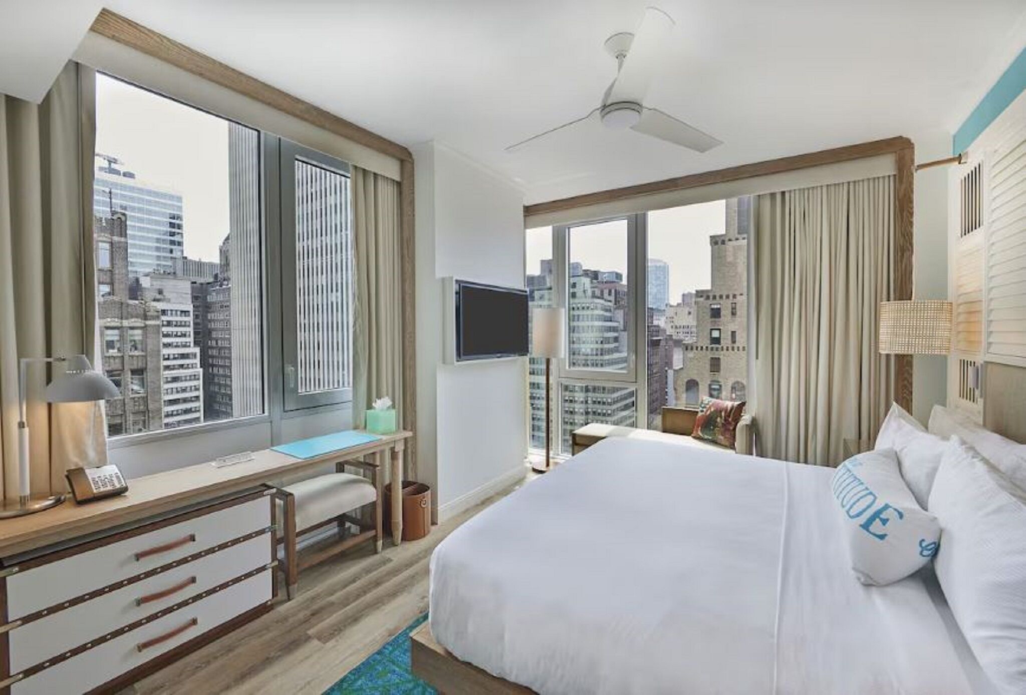 A hotel room with a large bed, a desk with a chair, a television, and a view of the cityscape.
