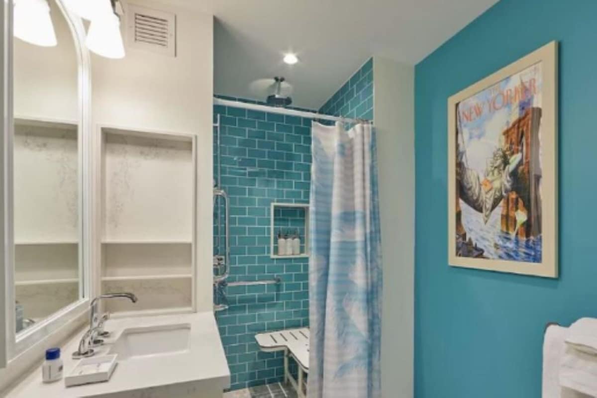 A bathroom with a white sink, a mirror, a shower with blue tiles, and a towel rack.