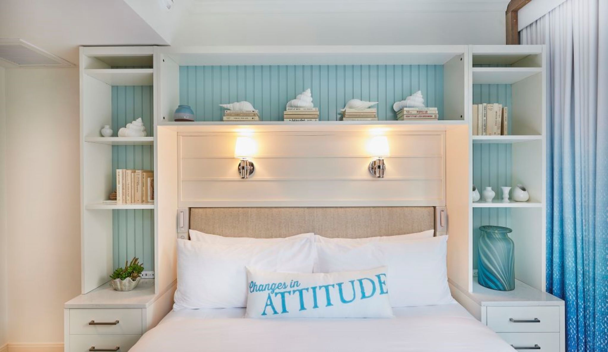 A neatly organized bedroom with a bed, bedside tables, a nightstand, a headboard, and built-in shelving with books and decorative items.