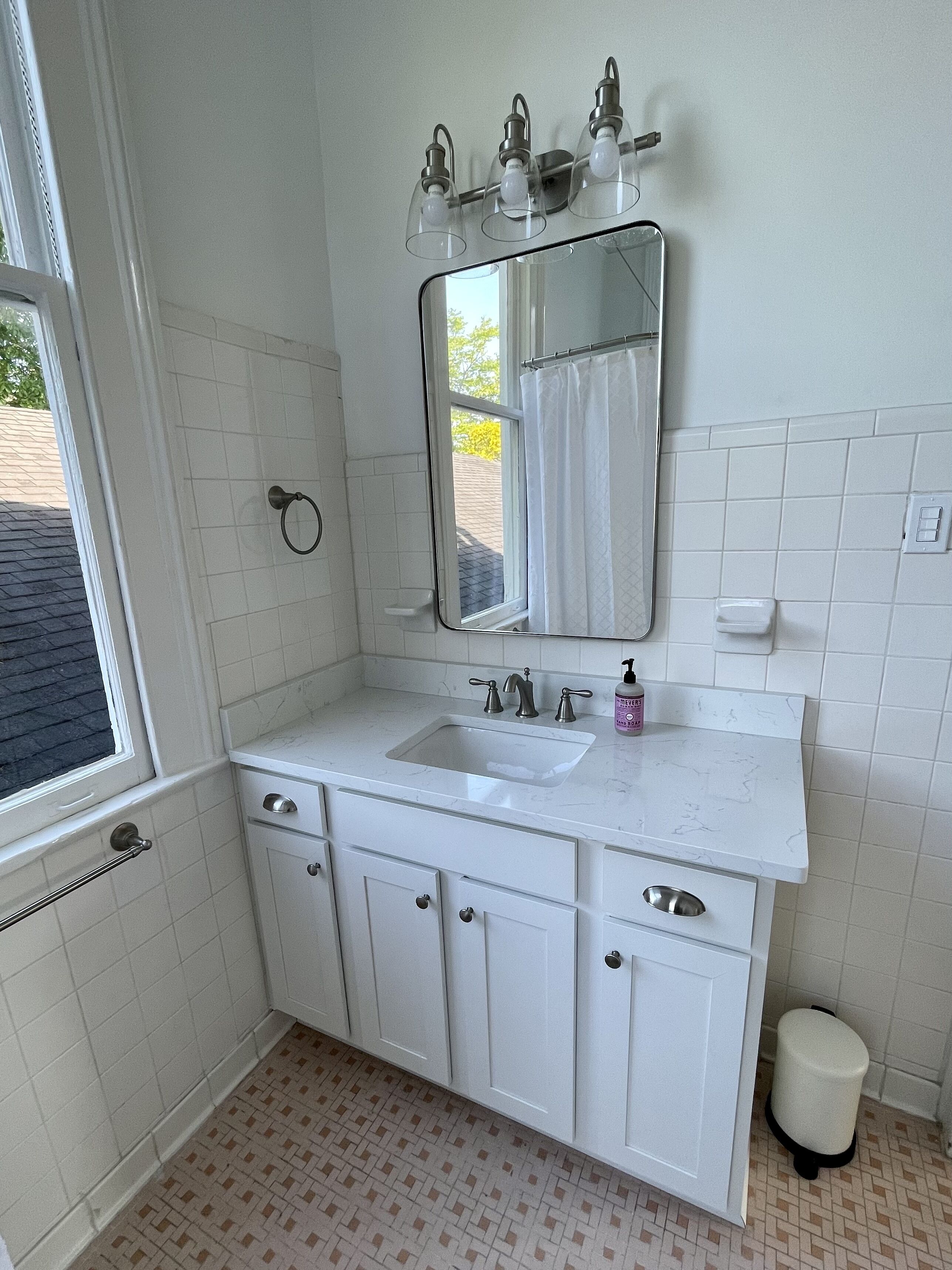 Un bany amb un moble de bany blanc, un lavabo, un mirall i una finestra.