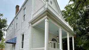 Une maison blanche de style colonial, dotée d’un porche à l’avant, d’un escalier en briques et d’un petit jardin.