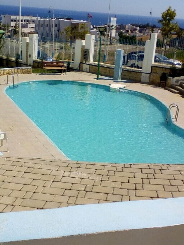 A rectangular swimming pool with a brick deck and metal railings, surrounded by buildings and a clear view of the sea. - Apartment - Summer Private Residence with Swimming Pools (M'diq)
