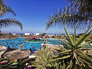 A large outdoor swimming pool surrounded by palm trees and umbrellas, with people swimming and sunbathing. - Apartment - Summer Private Residence with Swimming Pools (M'diq)